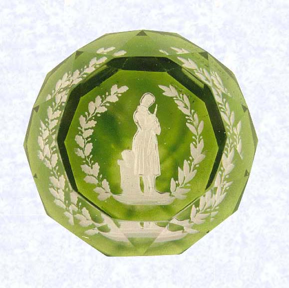 <B>Joan of Arc Sulphide<BR>France<BR>Baccarat, 1845-55</B><BR>Diameter: 8.9 cm (3 1/2 inches)<BR>(702263)<BR><BR>Sulphide scene of Joan of Arc, shown standing holding her sword, her helmet resting on a stand behind her; partially encircled by a wreath of oak and laurel leaves; set on a translucent emerald green base; sides cut with triangular facets; ten-sided facet cut on top