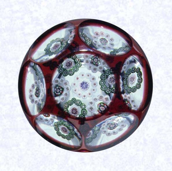 <B>Red Overlay<BR>France<BR>Baccarat, circa 1845-55</B><BR>Diameter: 7.3 cm (2 7/8 inches)<BR>(702294)<BR><BR>Single overlay of translucent ruby red, enclosing a garland millefiori design comprised of seven circlets; lower sides cut with twelve oval printies; upper sides cut witih six circular printies, one on top