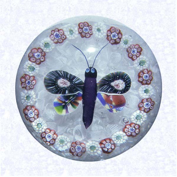 <B>Lampworked Butterfly on Filigree<BR>France<BR>Baccarat, circa 1845-55</B><BR>Diameter: 8 cm (3 1/8 inches)<BR>(702338)<BR><BR>Lampworked butterfly with deep purple body, black head, light blue eyes, and multicolored sliced millefiori cane wings; encircled by a ring of alternating red and white composite millefiori canes; on a white filigree ground