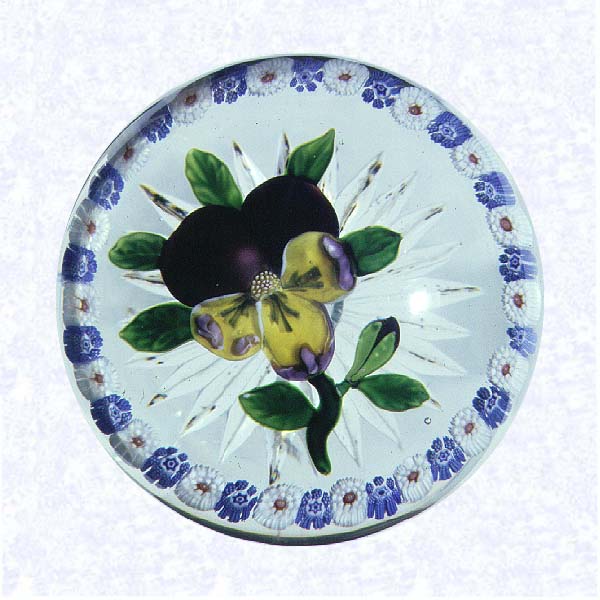 <B>Pansy with Millefiori Ring<BR>France<BR>Baccarat, circa 1845-55</B><BR>Diameter: 8.9 cm (3 1/2 inches)<BR>(702400)<BR><BR>Purple lampworked pansy with three yellow and purple lower petals and a purple bud; seven green leaves and stem; encircled by a ring of alternating blue and white millefiori canes; star-cut base