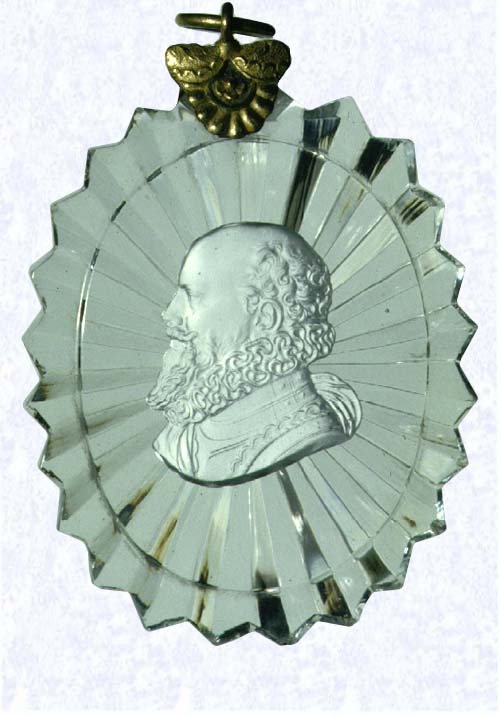 <B>Sulphide Portrait of Sixteenth-century Man<BR>France<BR>Baccarat, circa 1830</B><BR>Width: 5.7 cm (2 1/4 inches) Maximum Length: 9.2 cm (3 5/8 inches)<BR>(702466)<BR><BR>Oval clear glass plaque with serrated edges, enclosing a sulphide profile portrait of an unidentified man with a beard and neck ruff; sunburst cut on backside of plaque; gilded metal ring and collar