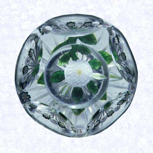 <B>Lampworked White Camomile<BR>France<BR>Baccarat, circa 1845-55</B><BR>Diameter: 7.3 cm (2 7/8 inches)<BR>(702249)<BR><BR>White lampworked camomile blossom with two white buds and pale green striped buds; yellow center cane; six green leaves and stem; encircled by a ring of alternating green and white millefiori canes; star-cut base; sides cut with five circular printies, one on top