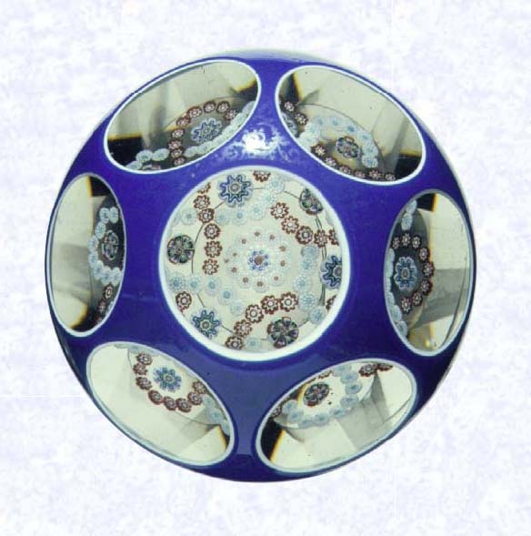 <B>Overlay with Garland Millefiori<BR>France<BR>Baccarat, circa 1845-55</B><BR>Diameter: 8.2 cm (3 1/4 inches)<BR>(702258)<BR><BR>Double overlay (opaque white overlaid with dark blue), enclosing a garland millefiori design comprised of two interlocked trefoils and isolated millefiori canes; overlay decorated with gilded scrollwork; sides cut with six circular printies, one on top