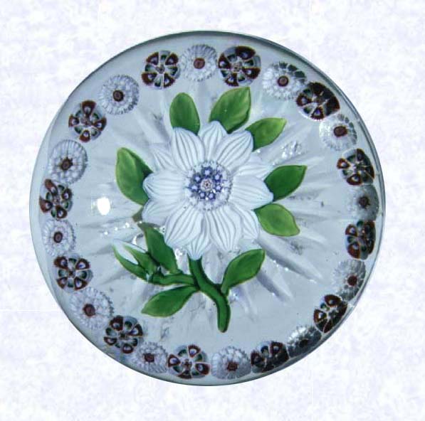 <B>White Clematis<BR>France<BR>Baccarat, circa 1845-55</B><BR>Diameter: 6.5 cm (2 1/2 inches)<BR>(702270)<BR><BR>Lampworked white clematis blossom with a white bud; blue and white center cane composed of star canes; nine green leaves and stem; encircled by a ring of alternating red and white millefiori canes; star-cut base