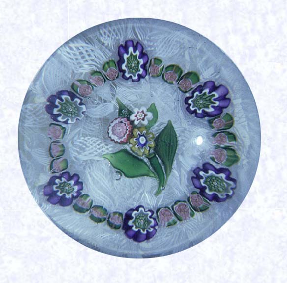 <B>Posy on Filigree<BR>France<BR>Clichy, circa 1845-55</B><BR>Diameter: 6.5 cm (2 1/2 inches)<BR>702309)<BR><BR> Posy of pink, yellow, and white raised millefiori cane flowers with four green lampworked leaves and stem; encircled by a ring of eighteen pink Clichy roses interspersed with six purple pastry-mold canes; on a white filigree ground backed with parallel rows of white filigree twists