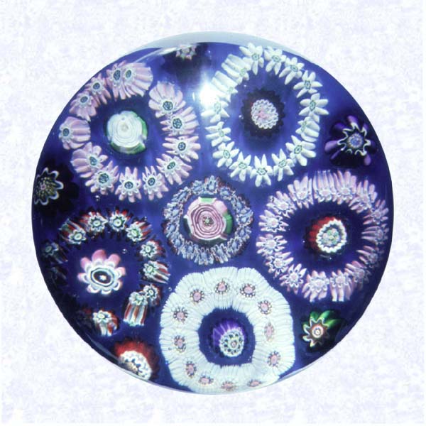 <B>Five-circlet Garland Millefiori<BR>France<BR>Clichy, circa 1845-55</B><BR>Diameter; 7.6 cm (3 inches)<BR>(702319)<BR><BR>Garland millefiori with five circlets in white, pink, and red canes, each containing a white Clichy rose; encircling a central blue and red circlet with a pink Clichy rose center; on an opaque blue ground; lower sides cut with nine four-sided printies tapering to the base