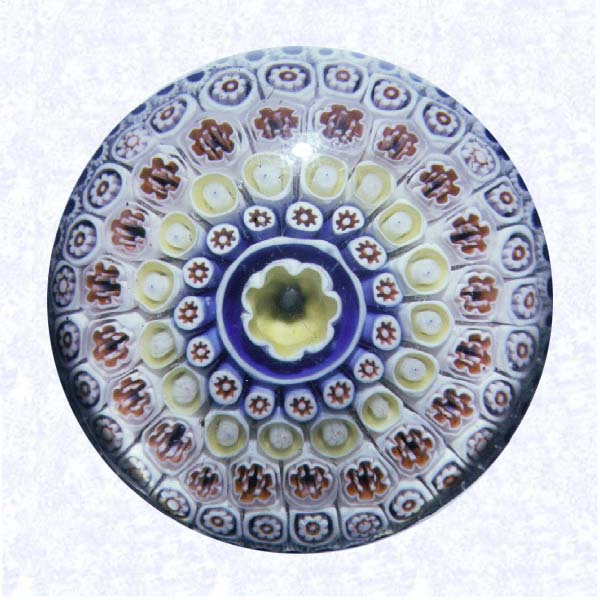 <B>Bacchus Close Concentric Millefiori<BR>England<BR>George Bacchus and Sons<BR>Union Glass Works, Birmingham, circa 1845-55</B><BR>Diameter: 8.6 cm (3 3/8 inches)<BR>(&02345)<BR><BR>Close concentric millefiori with five concentric rings of millefiori canes in white, blue, orange, and yellow encircling a large yellow-lined pastry-mold center cane