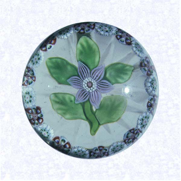 <B>Lampworked Lavender Clematis<BR>France<BR>Baccarat, circa 1845-55</B><BR>Diameter: 4.8 cm (1 7/8 inches)<BR>(702375)<BR><BR>Miniature weight with a lampworked lavender clematis blossom with a white and red center cane; five green leaves and stem; encircled by a ring of alternating red and white millefiori canes; star-cut base