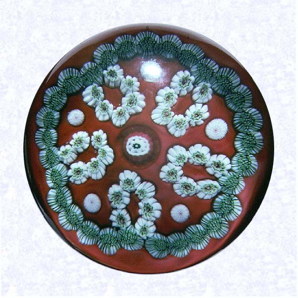 <B>Garland Millefiori on Red<BR>France<BR>Clichy, circa 1845-55</B><BR>Diameter: 7.6 cm (3 inches)<BR>(702435)<BR><BR>Garland millefiori with five white loops of white and green millefiori canes; single white canes spaced between loops; red and white center cane; on an opaque red ground